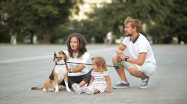 Çekici genç anne, baba sakallı, sevimli küçük kız ve Beagle köpek şehir meydanında onların aile hafta sonu birlikte sırasında oturuyorsun.