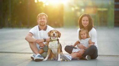 Küçük kız ve onların Beagle köpek şehrin yaz gün batımı sırasında ile genç aile açık havada portresi.