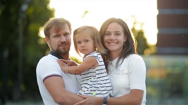 Na zewnątrz Portret młodej rodziny Lovely z córka. Przystojny ojciec trzymający mała dziewczynka na jego ręce. Matka brunetka przytulanie męża. — Wideo stockowe