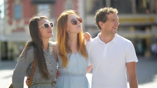 Un hombre guapo y dos chicas jóvenes atractivas conversando y sonriendo pasando tiempo juntos en la Plaza de la Ciudad Vieja en el soleado y cálido día al aire libre . — Vídeos de Stock