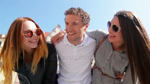 Nahaufnahme Porträt dreier junger Menschen am Altstadtplatz bei sonnigem, warmen Tag. Lächelnde Gesichter glücklicher Freunde, die Sommer und Sonne im Freien genießen. — Stockvideo