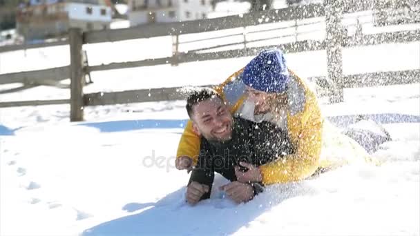 白い雪の中で横たわる抱き愛の若いカップルです。笑って幸せな人は、暖かい冬の天候を持つ楽しいアウトドア晴れた日の間に田舎. — ストック動画