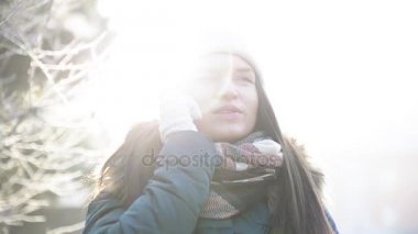 Genç gülümseyen kadın yanında Smartphone güneşli sabah açık havada biriyle konuşuyor. Güzel kız beyaz şapka ve Damalı eşarp kış manzara üzerinde cep telefonuyla konuşmayı.