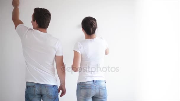 Vista trasera de la feliz pareja joven pintando la pared con pintura blanca en su sala de estar juntos . — Vídeos de Stock