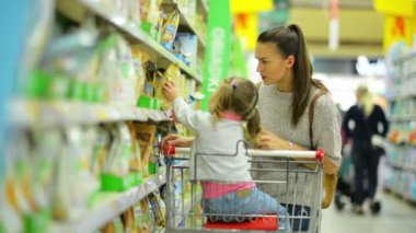 Kapalı genç çekici anne ve küçük çocuk gıda bir süpermarkette satın portresi. Mutlu aile ile alışveriş sepeti ürünlerini seçtiğiniz yan görünüm.