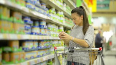 Harika esmer alışveriş sepeti sağlıklı bebek maması ürünler ile raf yakınındaki ayakta hipermarket içinde satın alma ile anne.