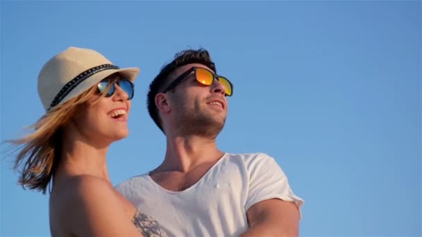 Közelkép a szabadban portréja, mosolygós boldog pár divatos napszemüveg a kék ég háttér, napos, szeles nap folyamán. — Stock videók