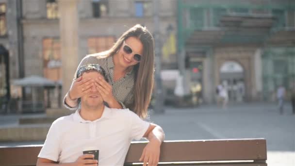 Bella bella donna in occhiali da sole chiude gli occhi per il suo fidanzato seduto sulla panchina sulla piazza della città durante la giornata estiva soleggiata . — Video Stock