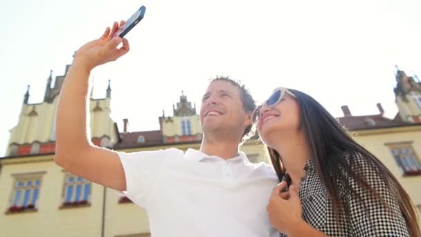 Szczęśliwi Podróżujący biorąc Selfie za pomocą smartfonu, stojąc na rynku starego miasta na tle budynków podczas słoneczny ciepły letni dzień. — Wideo stockowe