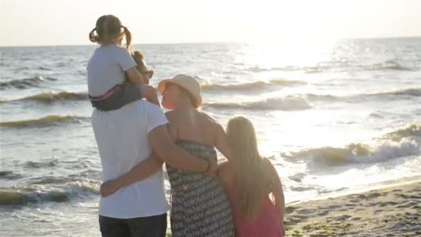 Weergave van mooie ouders en twee dochters uitgaven tijd samen in de buurt van de zee tijdens zonsondergang steunen. Knappe vader met één kind op zijn schouders. — Stockvideo