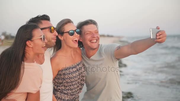 Retrato al aire libre de dos parejas tomando selfie por teléfono móvil en la playa durante el tiempo ventoso . — Vídeos de Stock