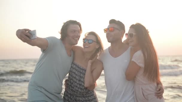 Πορτραίτο τεσσάρων φίλων λήψη Selfie χρησιμοποιώντας Smartphone μαζί στην παραλία κατά τη διάρκεια της φυσάει αέρας. — Αρχείο Βίντεο