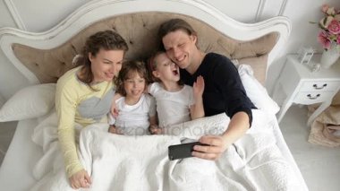 Selfie kullanarak akıllı telefon alarak neşeli ailedir. Sevimli erkek ve kız yatakta onların anne yalan öpüşme vardır.