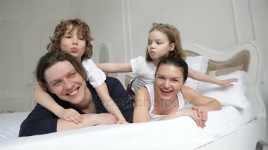 Mutlu anne ve iki çocuklar Lying beyaz yatak sahip eğlenceli birlikte sırasında hafta sonu evde vardır. Sevimli gülümsüyor, çocukları serbest zaman harcama ile genç Çift.