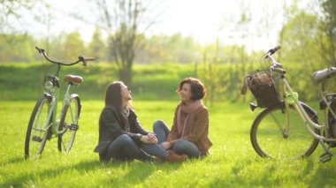 Çekici bayan arkadaşlar açık havada Bisiklet ve ağaçlar Parkı yeşil çimenlerin üzerinde oturan bir görüşme.
