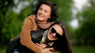 Sarılma kadın arkadaşı ile güneş gözlüğü oturan Her omuz sırasında bahar güneşli parkta oldukça kısa kıvırcık saçlı esmer.