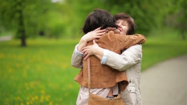 Erstaunliche Brünette umarmt ihre Mutter mit Liebe und Zärtlichkeit im Park. Porträt der erwachsenen Tochter und ihrer Mutter im Freien. — Stockvideo