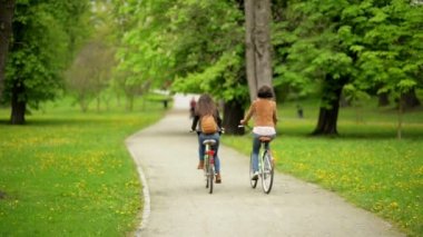 Bahar Park sırasında arka görünümü, iki esmer bisiklet ile at binme. Harcama zaman açık havada ceket ve kot komik aktif genç kadın vardır.