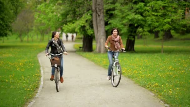 Leende damer på cyklarna ridning i parken under the Spring.Two aktiva flickor bär jackor och Jeans spendera tid tillsammans. — Stockvideo