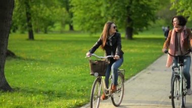 Kentsel Park iki güzel esmer ile büyüleyici Smiles bisikleti. İlk kadın kısa kıvırcık saçlı, giyen başka bir güneş gözlüğü vardır.
