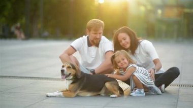 Güzel aile birbirine yere yaz günbatımı sırasında şehirde oturan sarılma. Beagle köpek sevimli Hugs, genç koca karısını öpüyor.