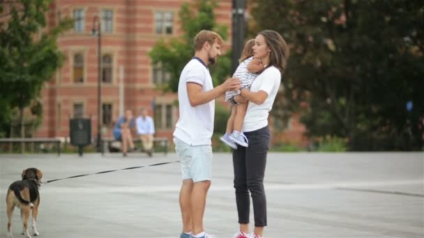 En plein air Portrait de famille heureuse avec Beagle Dog sur la place de la ville. Jeune mère tient sa fille sur les mains, fille en robe étreint sa mère . — Video