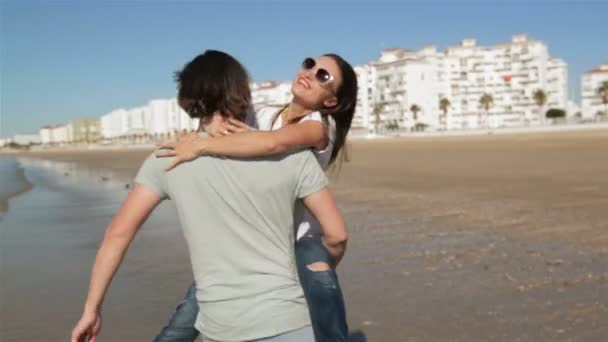 Joven pareja divertida en gafas de sol Piggybacking en la playa. Amigos juntos divirtiéndose. El mar está en el fondo . — Vídeos de Stock