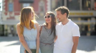 Uzun saçlı, güneş gözlüğü ve kısa elbiseler yakışıklı adam birlikte eski şehir merkezinde Beyaz gömlekli güneşli yaz gün boyunca eğleniyor iki sevimli kadın kentsel portresi.