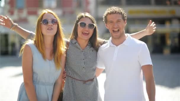 ファッショナブルなサングラスで 3 人の笑顔幸せな友人の肖像画は、都市の背景にカメラながらポーズ アウトドアと見ています。. — ストック動画
