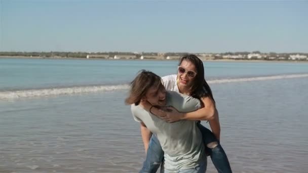 Jeune couple drôle dans des lunettes de soleil Piggybackking sur la plage. Amis ensemble s'amuser. La mer est sur fond . — Video