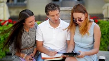 Önden Görünüm, iki çekici kız ve yakışıklı biri sınava birlikte şehir parkta bankta oturmuş sıcak güneşli gün boyunca açık havada hazırlanıyor. E-öğrenme kavramı.