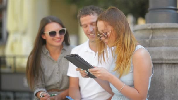 Groep jongeren met notities, pennen en Tablet tijd buiten doorbrengen. Openlucht portret van drie studenten praten en studie samen buiten zitten op de Bank. — Stockvideo