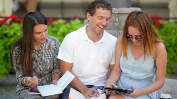 Due studentesse con un ragazzo che studia insieme all'aperto sedute sulla panchina del parco cittadino. Concetto di e-learning . — Video Stock