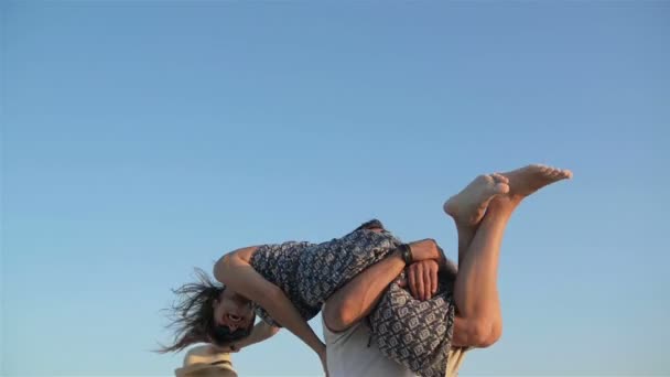 Na zewnątrz portret z Strong Man podnoszenia jego dziewczyna na ramionach i Swirling na niebieskim tle niebo. Kobiety w długiej sukni, śmiejąc się i trzyma kapelusz lato w ręce. — Wideo stockowe