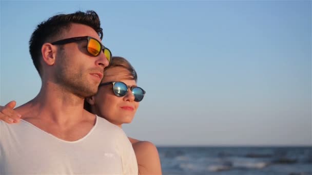 Vista lateral del encantador hombre y la mujer en gafas de sol de moda en el fondo del cielo azul durante el soleado día ventoso . — Vídeos de Stock