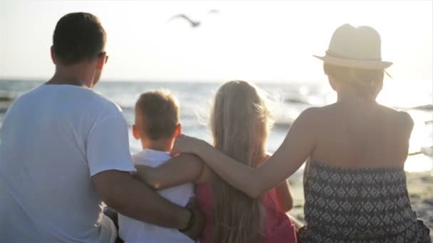Weergave van mooie familie knuffelen in de buurt van de zee en kijken terug op de zon en de golven. — Stockvideo