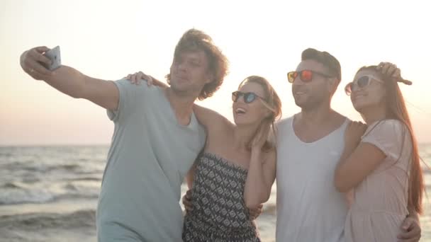 Ritratto di quattro persone con bianchi sorrisi dentati che scattano selfie dal telefono cellulare Trascorrere del tempo insieme sulla spiaggia durante il tempo ventoso . — Video Stock