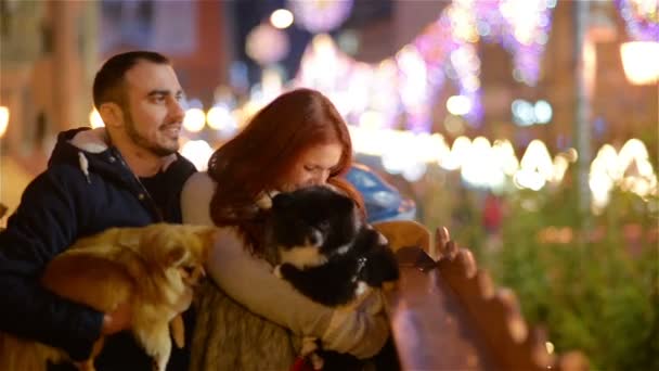 Молодая пара с белой внешностью развлекается с парой собак. Огни и Рождество на заднем плане . — стоковое видео