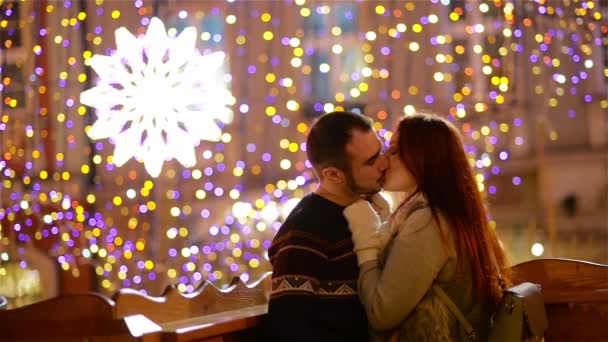 Romantisches Paar mit kaukasischem Aussehen, das sich küsst und kuschelt. Lichter und Feuerwerk sind im Hintergrund zu sehen. junges Paar, das diese romantische Nacht mit sich selbst verbringt. — Stockvideo