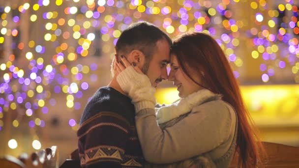 Romantisches Paar mit kaukasischem Aussehen, das sich küsst und kuschelt. Lichter und Feuerwerk sind im Hintergrund zu sehen. junges Paar, das diese romantische Nacht mit sich selbst verbringt. — Stockvideo