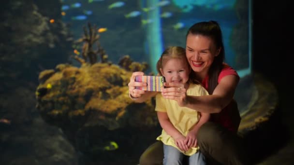 Glückliche Mutter und Tochter machen Selfie. Aquarium mit Fischen im Hintergrund. Sie haben viel Spaß an diesem Muttertag. — Stockvideo
