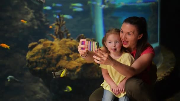 A mãe e a filha felizes estão a levar a Selfie. Aquário com peixes está no fundo. Eles se divertem muito neste dia das mães . — Vídeo de Stock