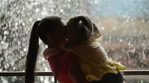 甘い小さな女の子は抱きと彼女の美しい若いお母さんのキスです。幸せな母の日。滝の背景には. — ストック動画