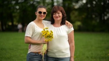 Parkta yetişkin kızı ile gülümseyen olgun bir kadın portresi. Anneler günü kutlama var. Arka plan üzerinde yeşil çimen mi