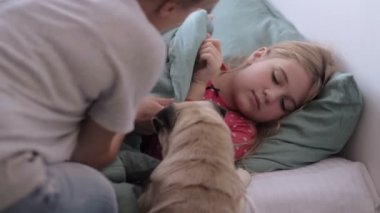 Anne hasta bir çocuğa bakıyor, gripten yatıyor, termometreyi kullanıyor, ateşi olan bir kız evdeki kanepede tatlı bir köpekle yatıyor, Aile Tedavisi.