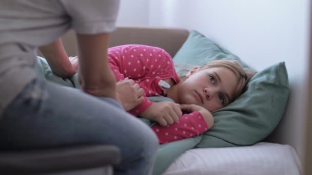 Η μητέρα δίνει ψηφιακό θερμόμετρο στην μικρή κρύα κόρη της, ξαπλωμένη σε έναν καναπέ στο σπίτι. — Αρχείο Βίντεο
