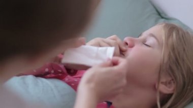 Anne soğuk küçük kızına dijital termometre veriyor. Evdeki kanepede yatıyor.