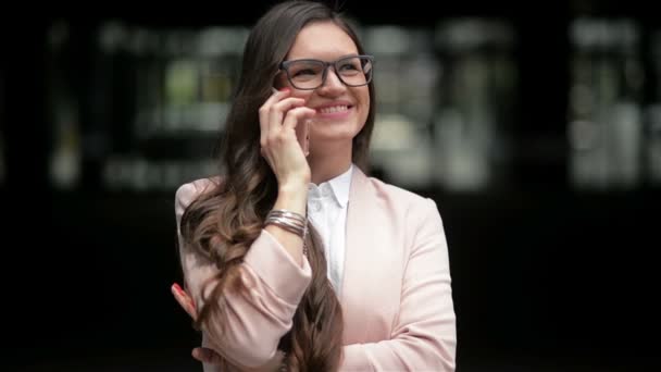 Happy Young Lawyer está falando ao telefone em pé no prédio da cidade fundo. Morena bronzeada em jaqueta branca está discutindo negócios com sorriso alegre ao ar livre. Conceito: Pessoa de negócios, Profissional — Vídeo de Stock