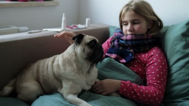 Sick little beautiful girl with a scarf and a her pug dog in bed. Near the girl are medicines: a spray for the nose, cough and throat pills, an electronic thermometer. — Stock Video