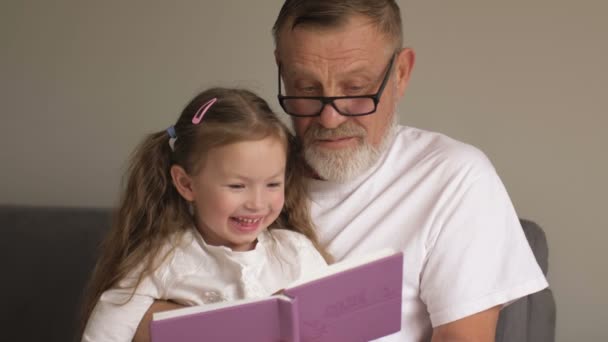 Nagyapa könyvet tanít az unokájának. Családi nevelési koncepció. Egy idős férfi és egy kislány egy tankönyvet lapoz át.